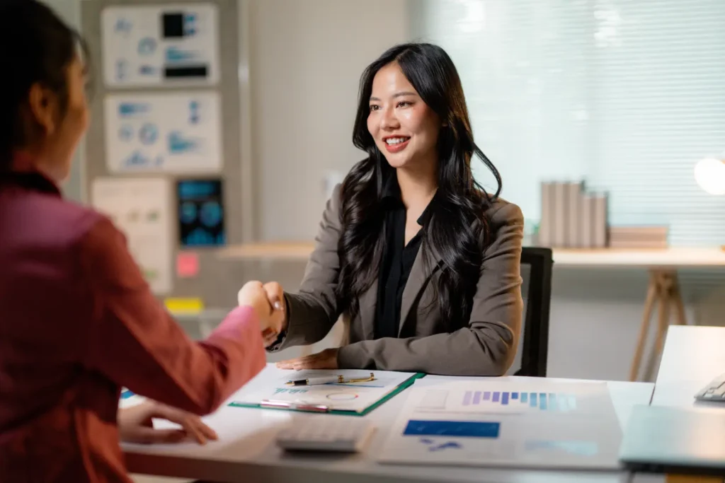 a businesswoman happily shaking hands with another businesswoman after acquiring a business through m&a support